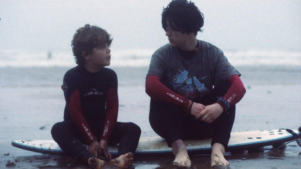 Two boys from My Brother is a Mermaid sat on a surfboard