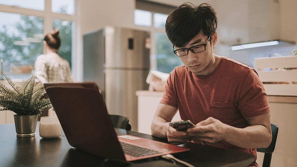 Man looking at phone and laptop