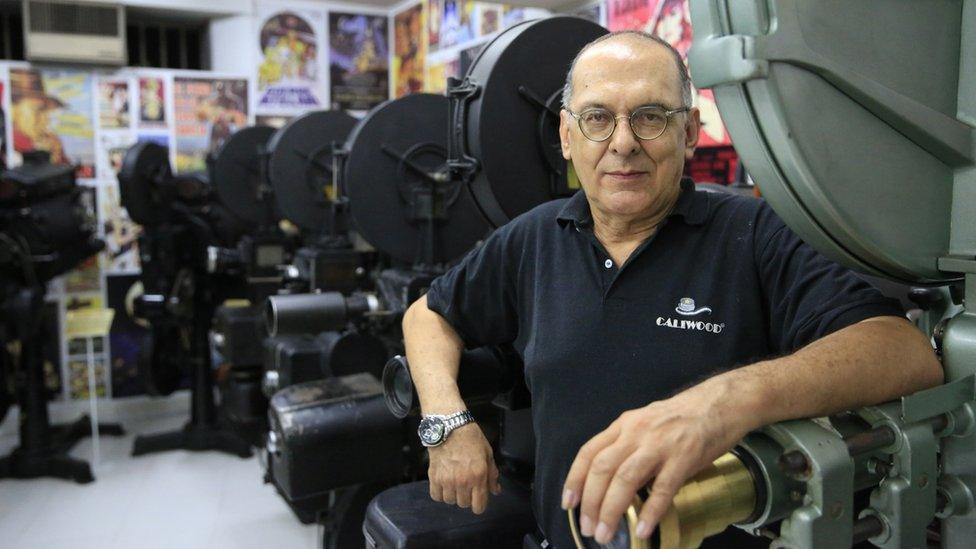 Hugo Suarez poses in front of a green Iskra Kranj KN-3 35mm projector from 1963