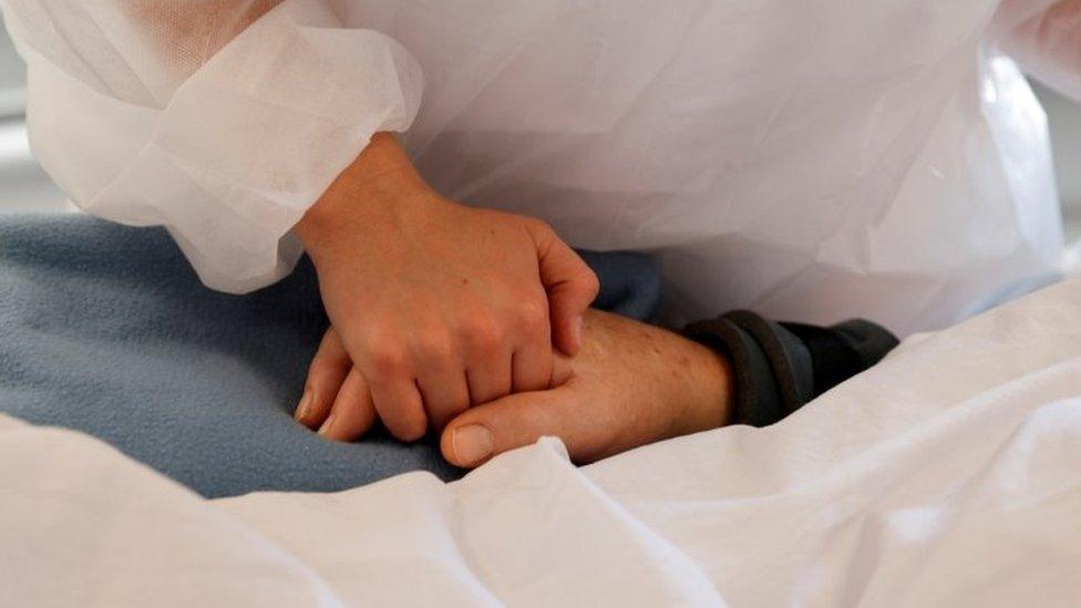 A nurse holds the hand of a man in hospital