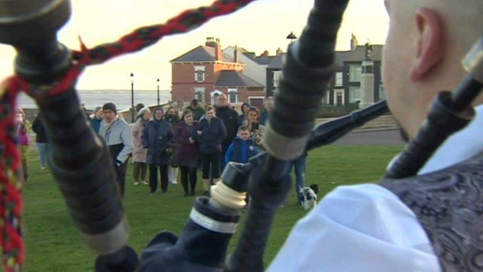 A crowd looks on as Chris Pearson plays the bagpipes