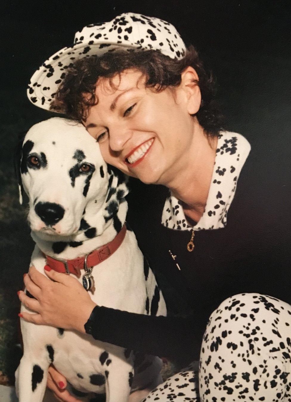 Cat Hulbert cuddling a dog, wearing spotty trousers and matching baseball cap