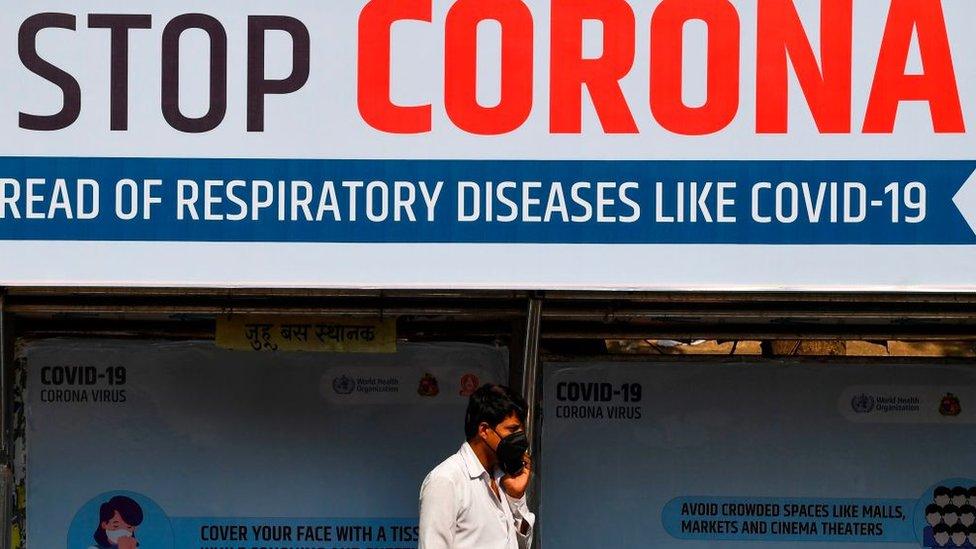 An Indian man wearing a face mask walks past a giant sign reading "stop Coronavirus"