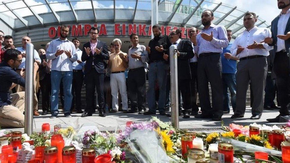 People pray at a memorial of candles and flowers in front of the Olympia shopping centre in Munich where Friday's shooting happened (24/07/2016)