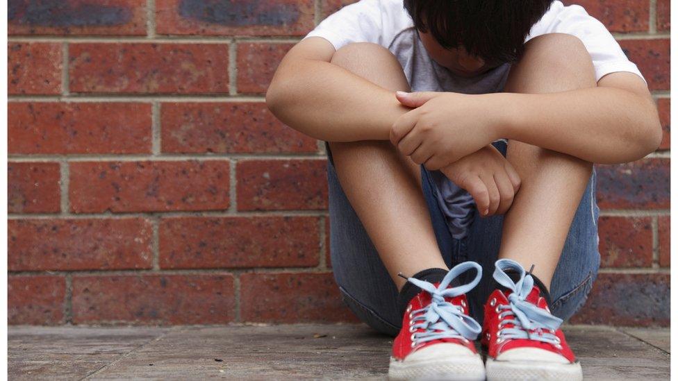 Boy sitting against a brick wall with his head down