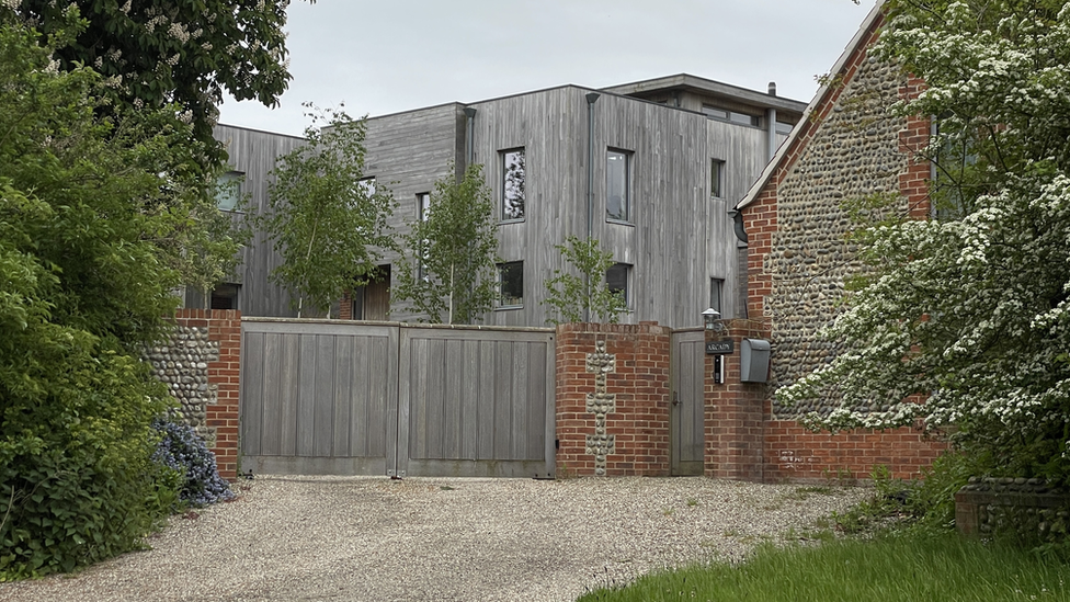 Arcady house, showing wooden structured house behind closed wooden gate and gravel driveway