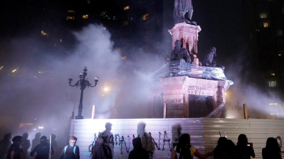 Demonstrators stand next to a vandalised monument during a protest against femicide and violence against women, in Mexico City, Mexico, 25 November, 2019.