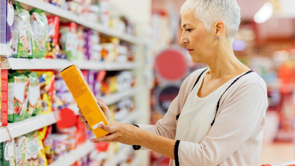 A woman reads the labelling on the back of a cereal box in a shop.