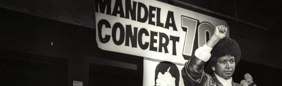 Winnie Mandela raises her fist in a black power salute after announcing that a massive pop concert will be held to mark the 70th birthday of her husband in 1988