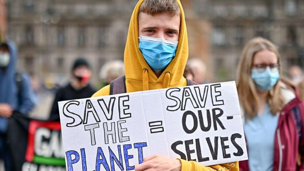 A protestor holds a placard saying 'Save Our Planet = Save Our Selves'