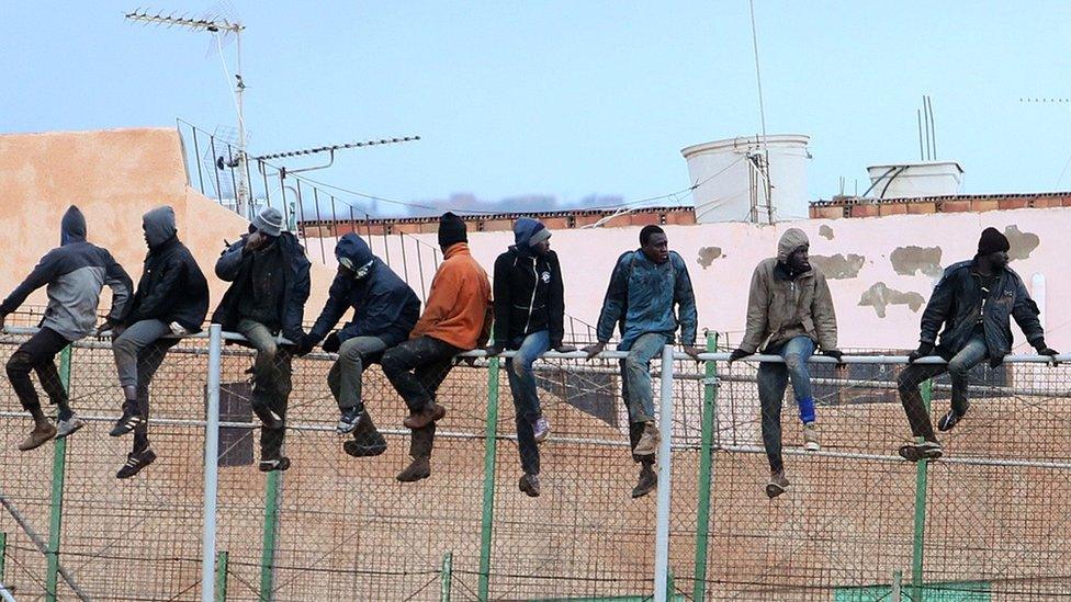 Migrants sit atop a border fence separating Morocco from Spanish enclave of Melilla, 19 Feb 15