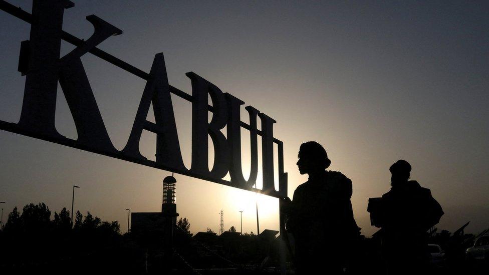 Taliban soldiers stand in front of a sign at the international airport in Kabul in 2021