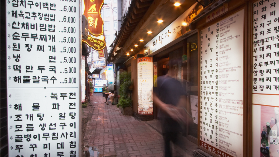 A man walking past a Korean restaurant with large menu boards outside in Seoul