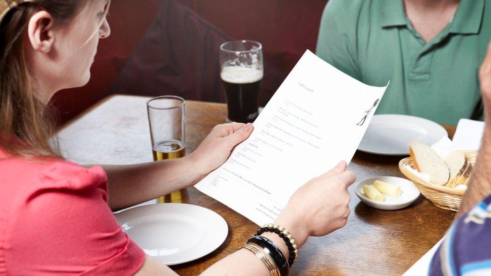 A woman holds a menu at a restaurant table