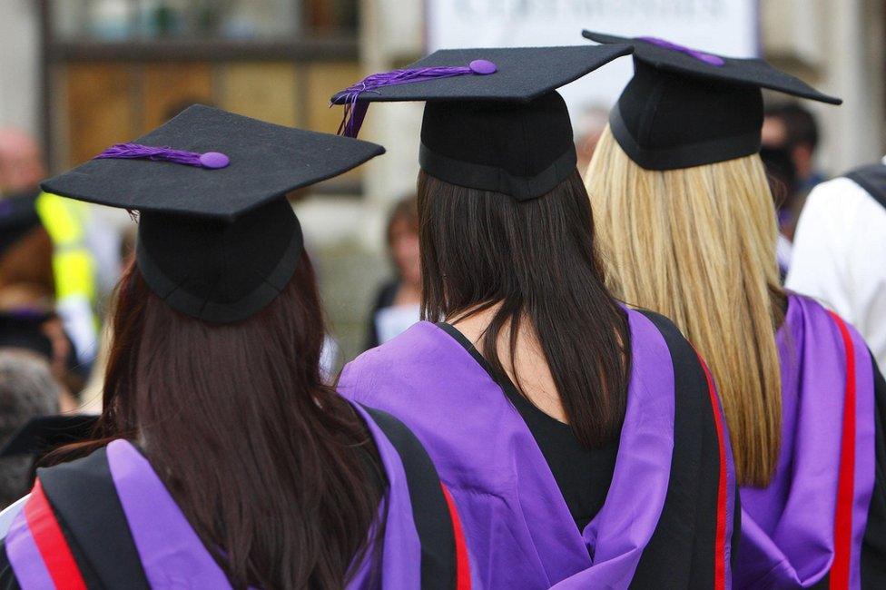 Three university graduates in mortar boards and purple gowns