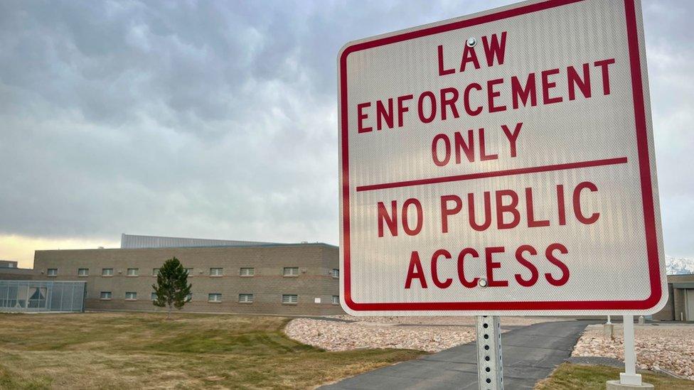 In the foreground a sign reading 'law enforcement only no public access' in red text and in the background, a large stone building fronted backed by mountains