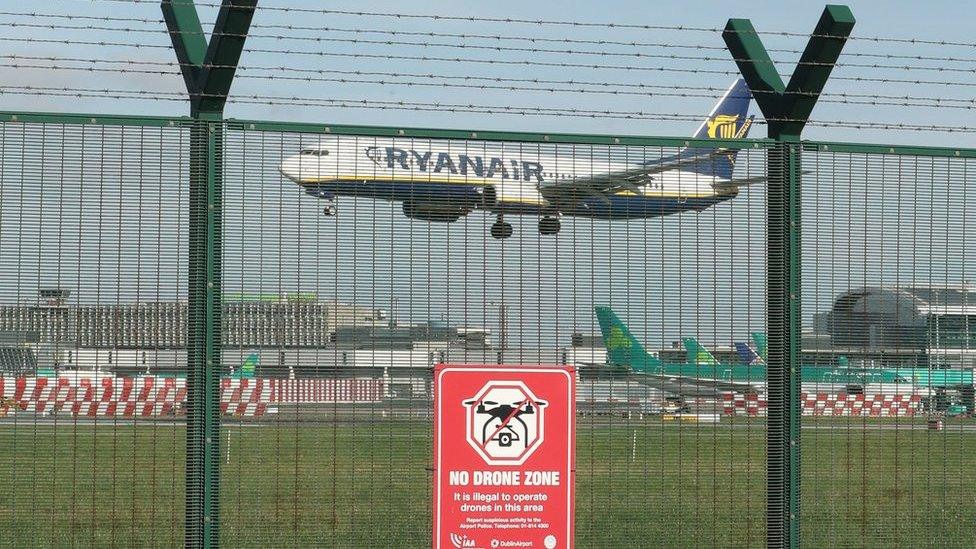 A plane flying into Dublin Airport behind a fence with a sign that reads: No drone zone