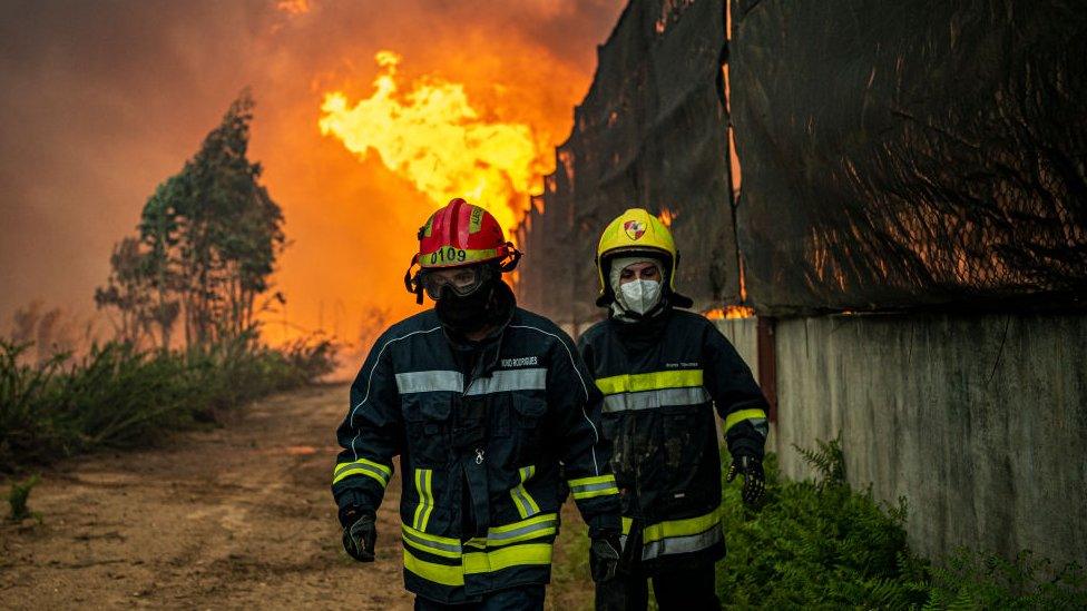 two firefighters walking away from a large outdoor fire