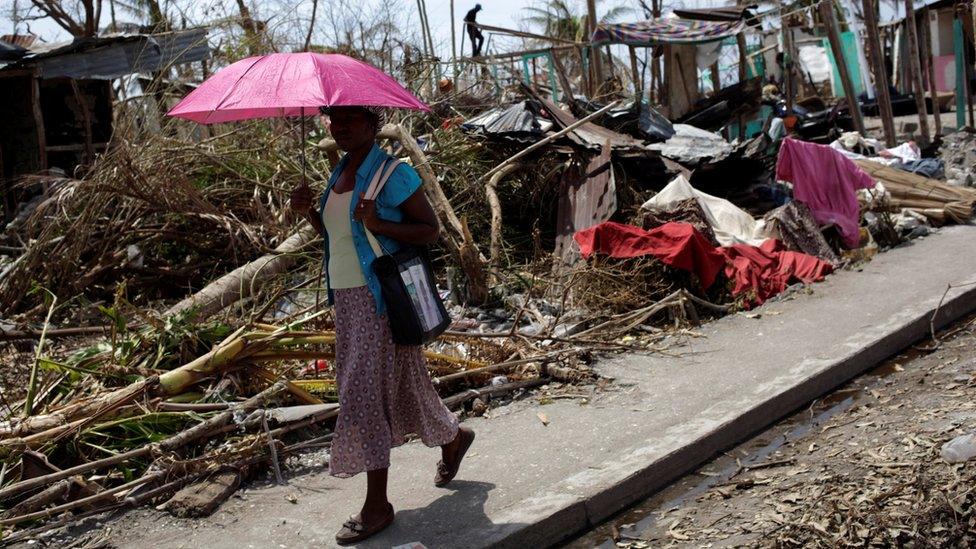 A woman holds an umbrella as she walks next to houses destroyed by Hurricane Matthew in Les Anglais