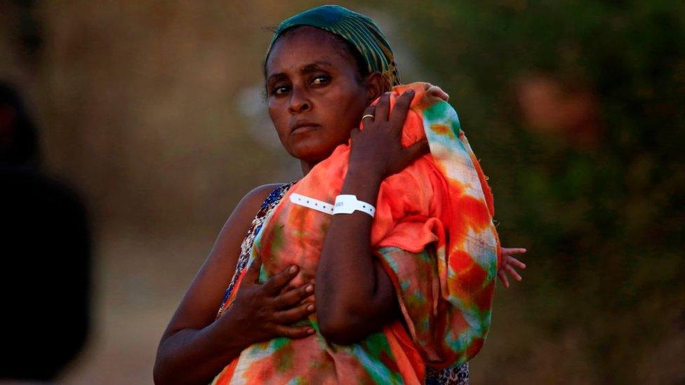 An Ethiopian refugee who fled fighting in Tigray province carries her baby as she walks at the Um Rakuba camp in Sudan's eastern Gedaref province