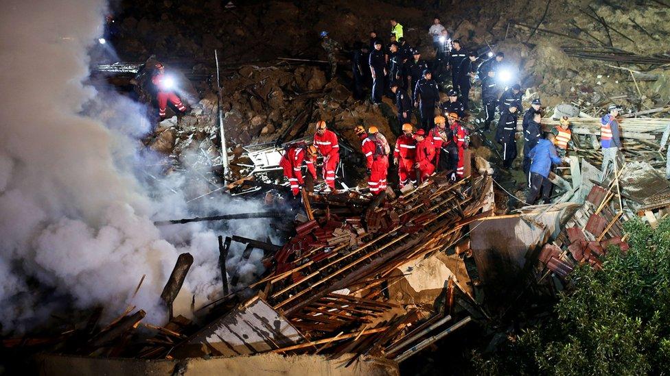 Emergency services personnel clambering on top of building wreckage and mud