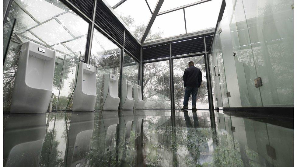 Man standing next to row of urinals in the glass room. Changsha, China, 29 September 2016.