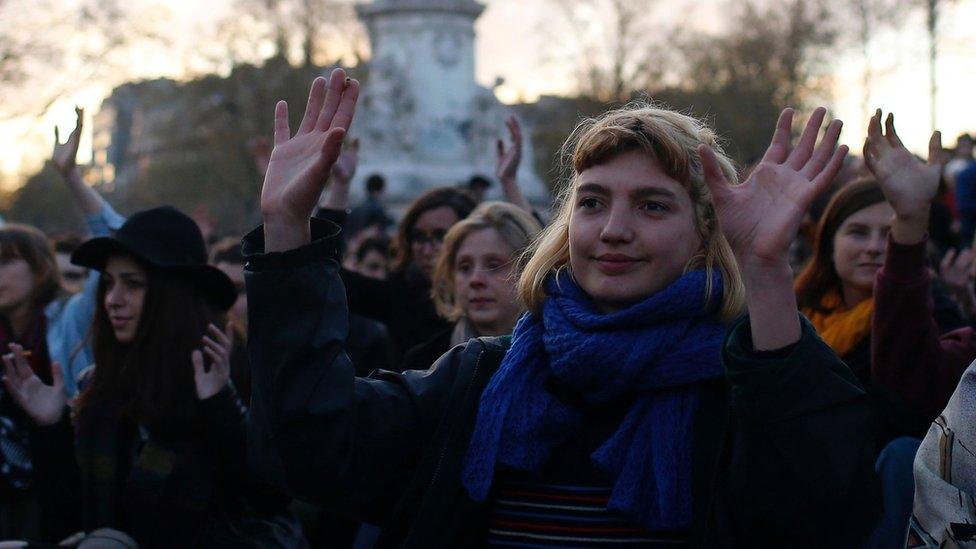 People gesture as they listen to a speech during a gathering by the 'Nuit Debout' movement on Place de la Republique in Paris