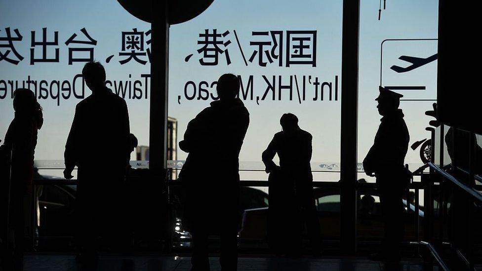 Travellers stand near the international departures area at the airport in Beijing on February 6, 2016