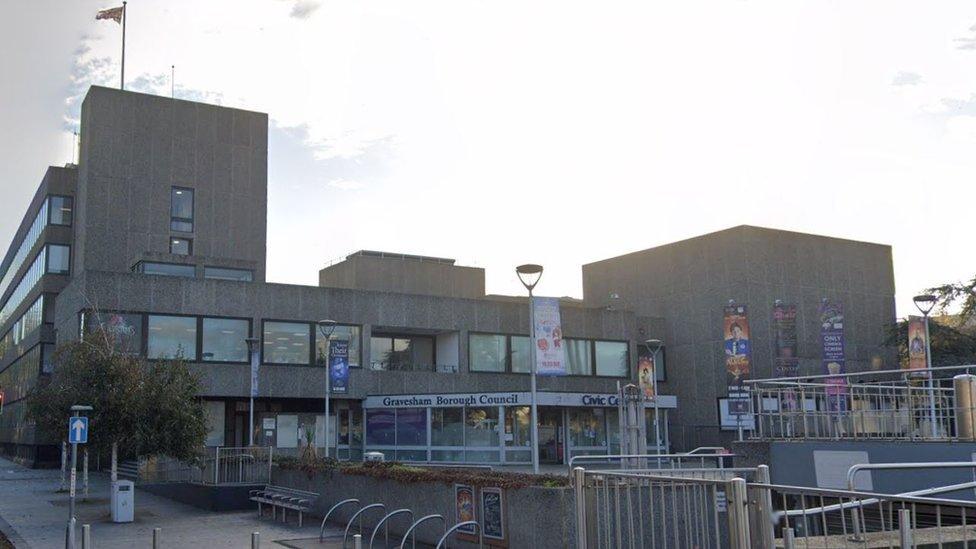 A large concrete building with Gravesham Borough Council written across the front and the sun shining from behind it