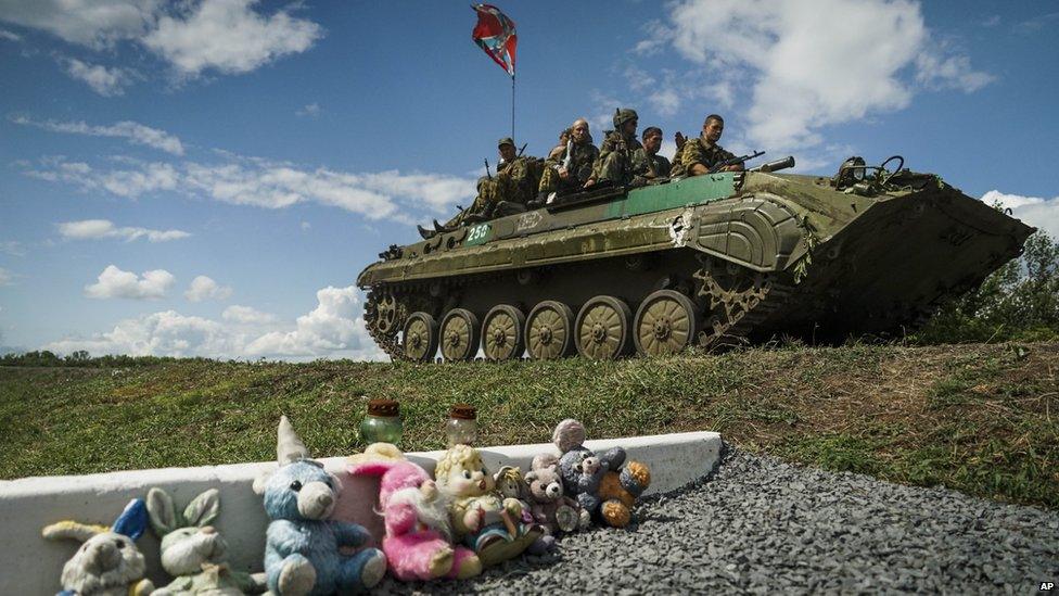 Ukrainian separatist APC, with a flag of the self-proclaimed Federal State of Novorossiya, rides by a memorial to victims of the Malaysian Airlines MH17