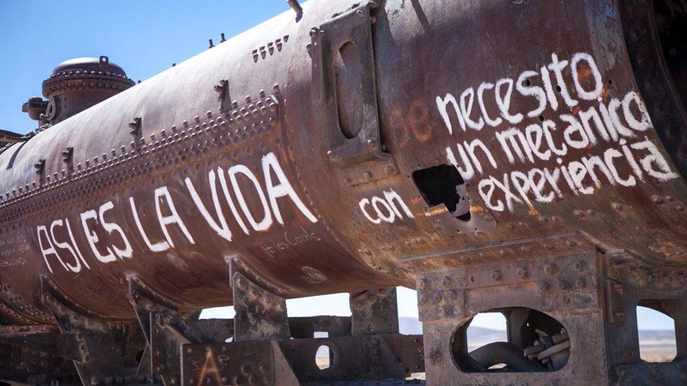 Graffiti on the side of an abandoned train reads "Life's like that" and "I need an experienced mechanic"