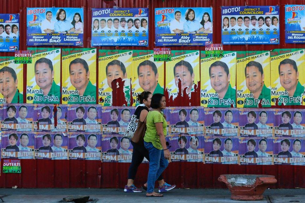 Two Filipinos walk past a wall covered with election posters in Makati on 4 May