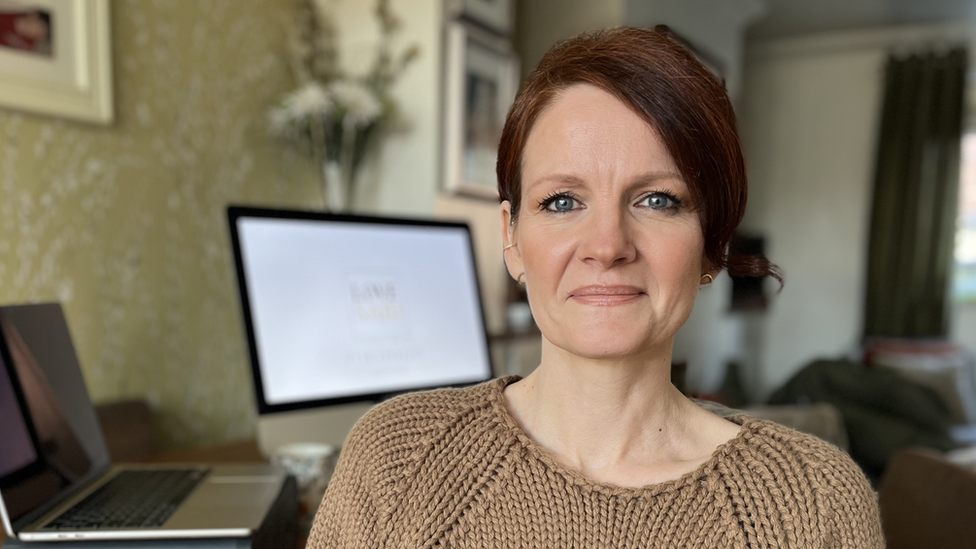 Anna Rowe in a beige jumper sitting by a desk