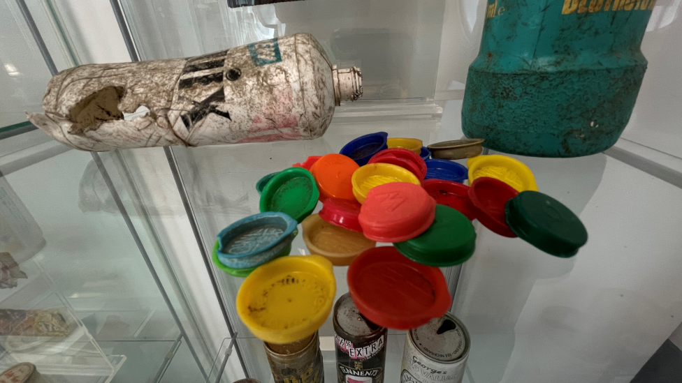 A collection of bottle caps, a while plastic bottle and a blue bottle