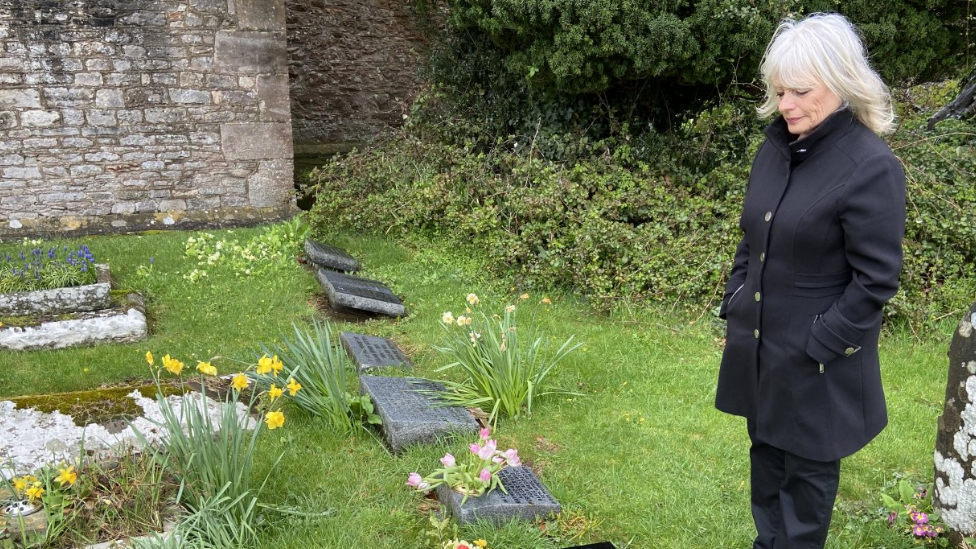 Jacki Sutton looking down at graves in a cemetery wearing all black