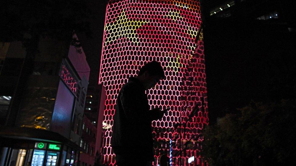 A man looks at his phone near a giant image of the Chinese national flag on the side of a building in Beijing in 2017