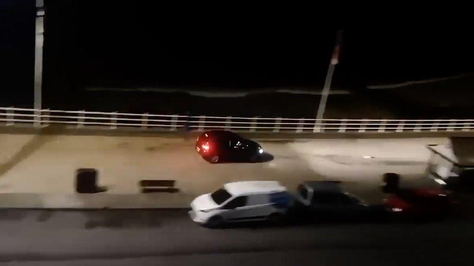 A black car driving along the seafront