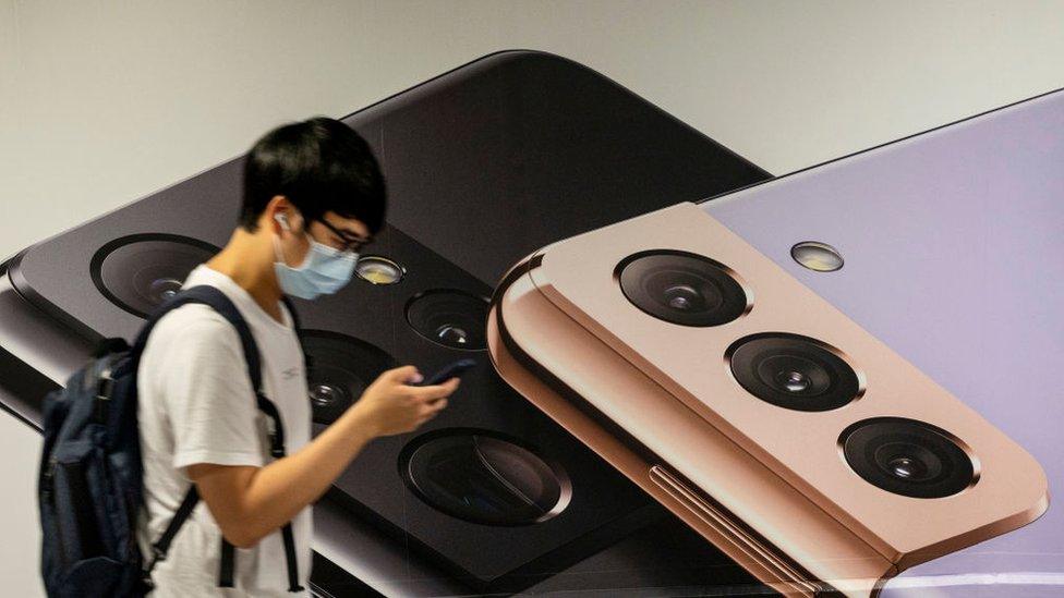 A man uses a smartphone as he walks past the South Korean multinational electronics Samsung advertising the Samsung Galaxy s21 5G smartphone on a billboard in Hong Kong.