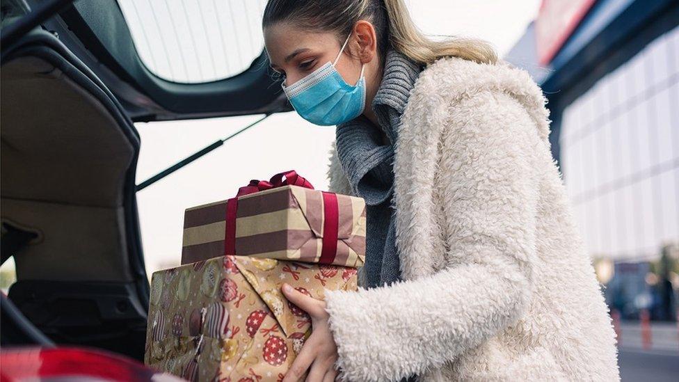 Woman wearing face covering puts presents in a car