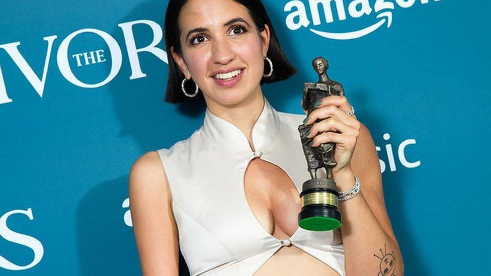 Victoria Canal with her award, in a white dress, smiling at the camera