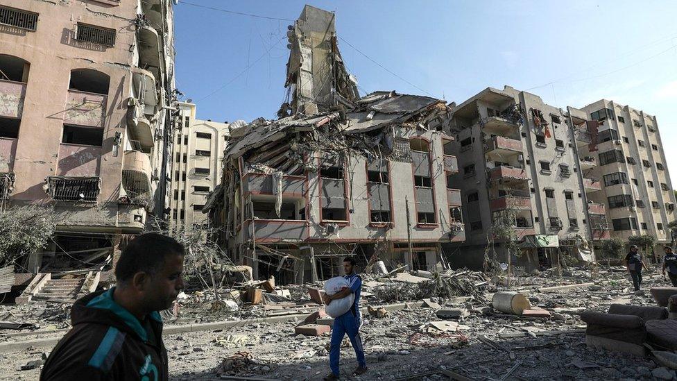 Palestinians walk past damaged buildings in Gaza City's Tal al-Hawa district (30 October 2023)