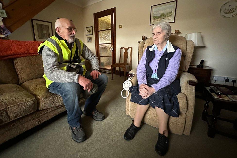 A man on a sofa talks to a woman in an arm chair