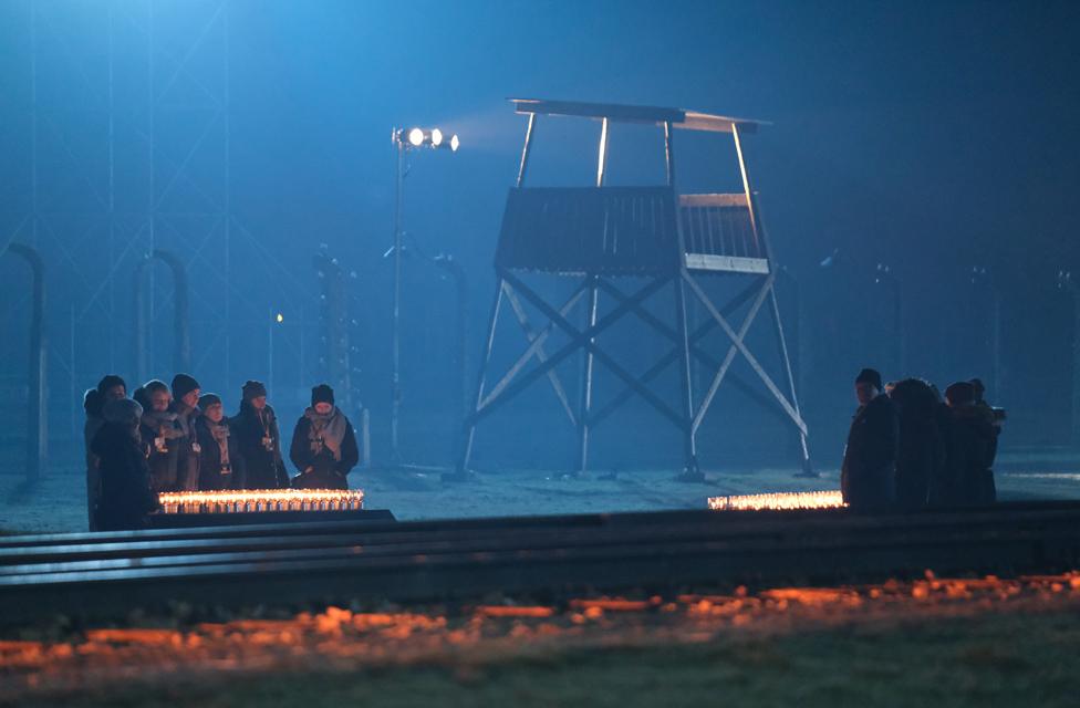 Participants stand at candles near the railroad tracks and an illuminated guard tower at the former Auschwitz-Birkenau concentration camp during the official ceremony to mark the 75th anniversary of the liberation of the camp.