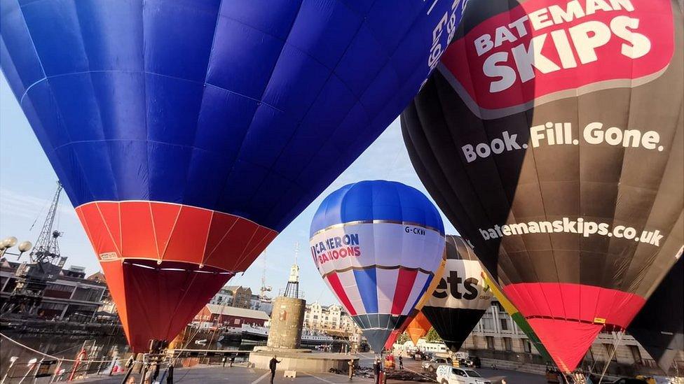 Hot air balloons being inflated at Bristol's harbourside, including a black and red balloon