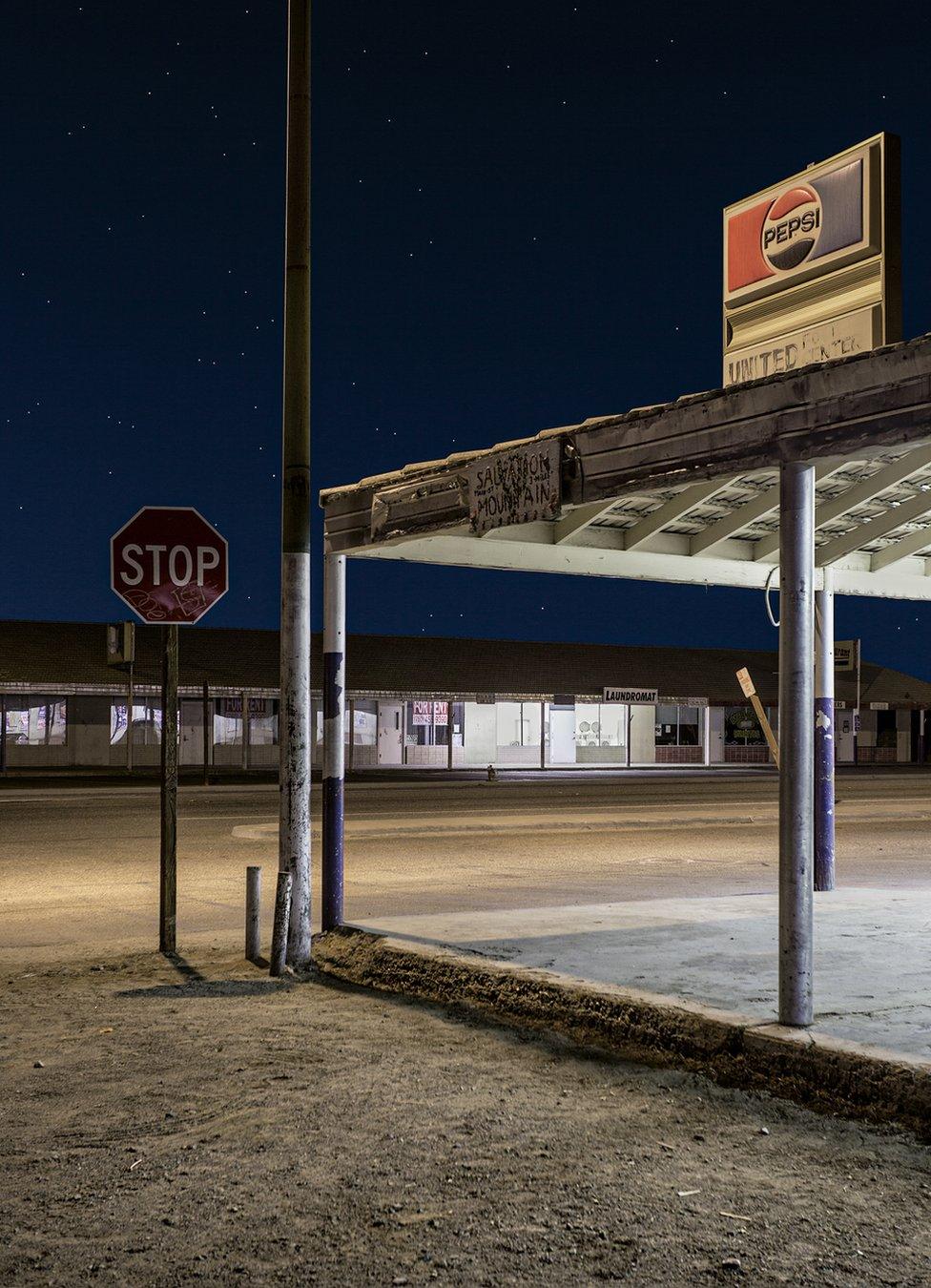 A night view of an abandoned fuel station in an empty street under a starlit sky