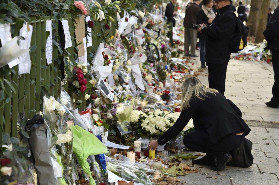 A woman lights a candle in front of a makeshift memorial near Bataclan