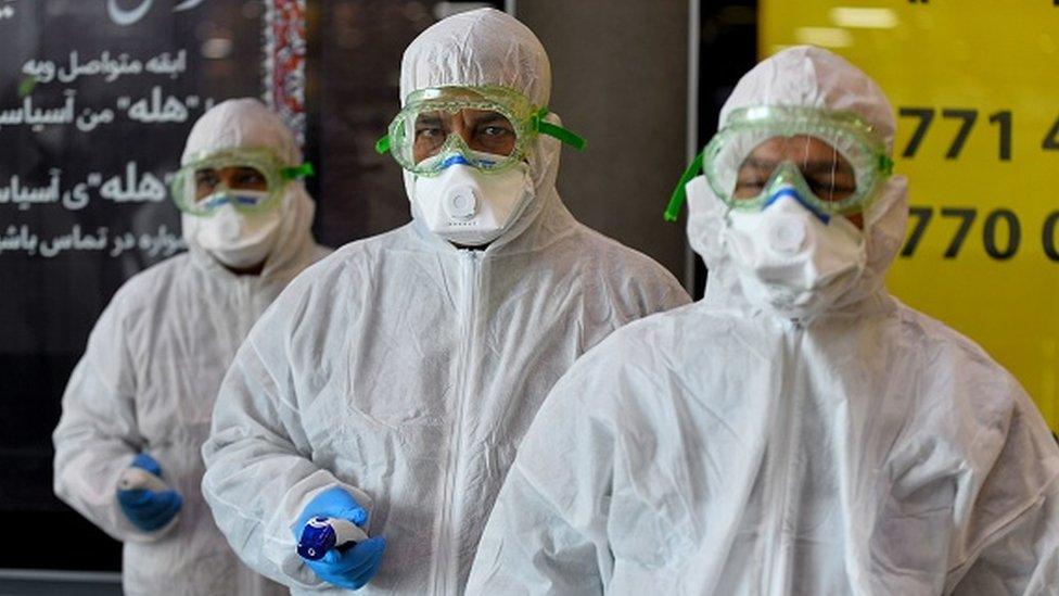 A medical team wearing protective outfit awaits to check Iraqi passengers returning from Iran