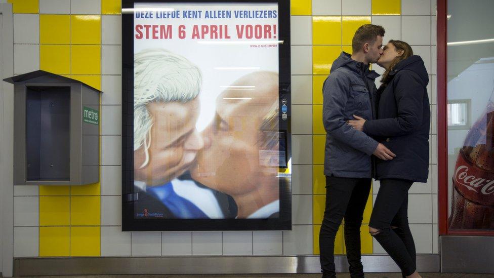 A couple stands next to a poster depicting Dutch politician Geert Wilders and Russian President Vladimir Putin kissing (3 April)