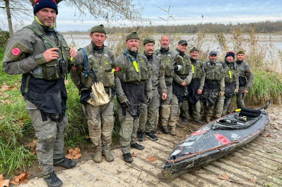 Men stand next to a kayak