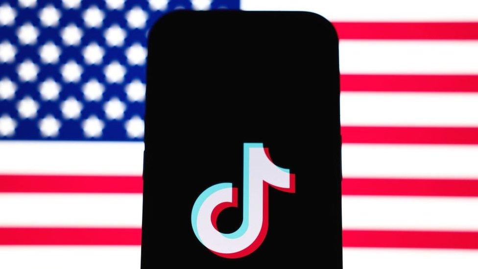 TikTok's logo displayed on a smartphone, with the US flag in the background